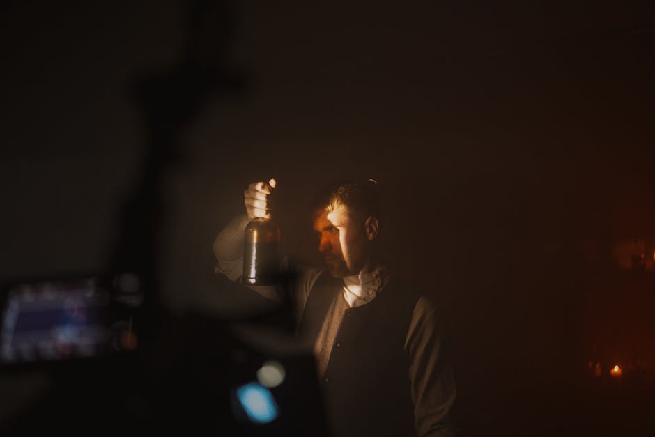 Moody portrait of a man in dim lighting holding a bottle, evoking mystery.