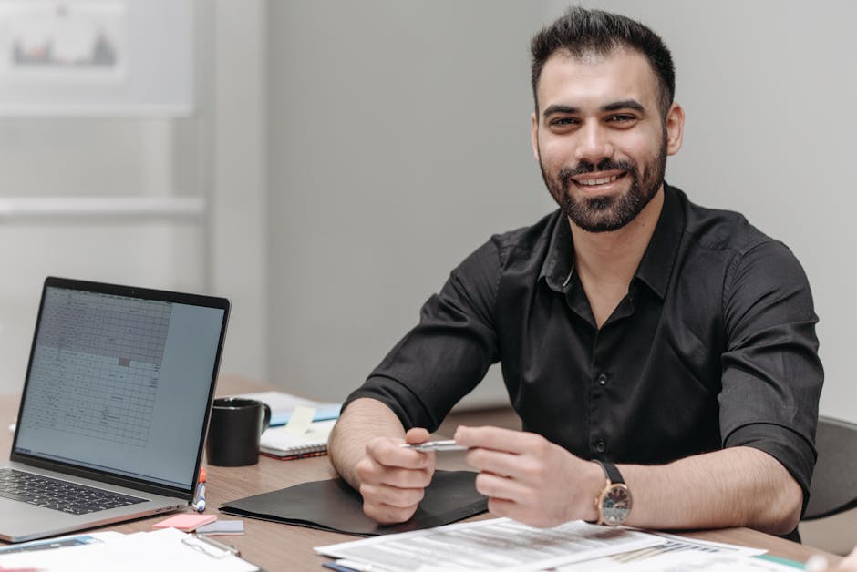 Confident businessman sitting at desk with laptop and documents, ready for a meeting.