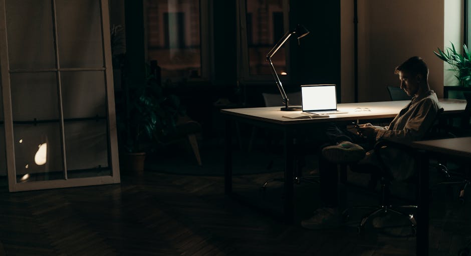 A man using his laptop in a dimly lit office at night, highlighting a dedicated work environment.