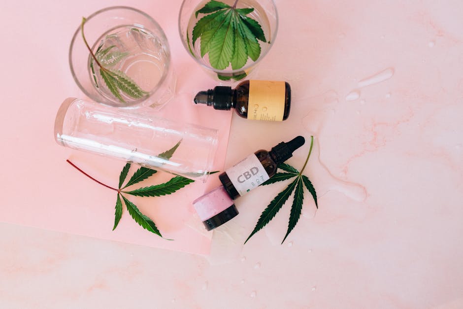 Flat lay of CBD oil bottles and cannabis leaves on a pink surface, emphasizing wellness products.