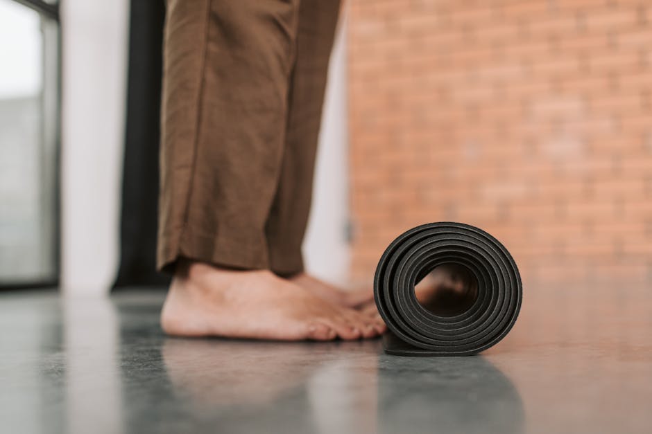 A person standing barefoot by a rolled yoga mat indoors, ready for exercise.