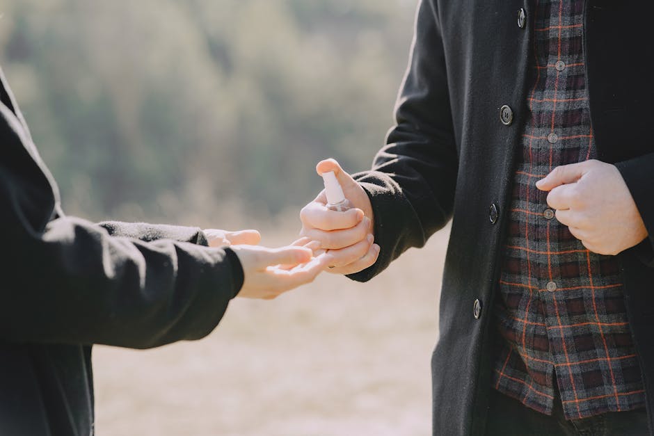 Crop anonymous couple in outerwear wiping off hands with antiseptic to prevent coronavirus spreading while strolling together in sunny countryside