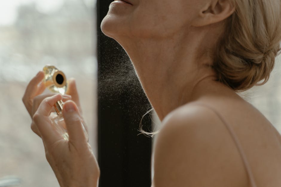 Close-up of a woman applying perfume with a glass bottle in natural light.