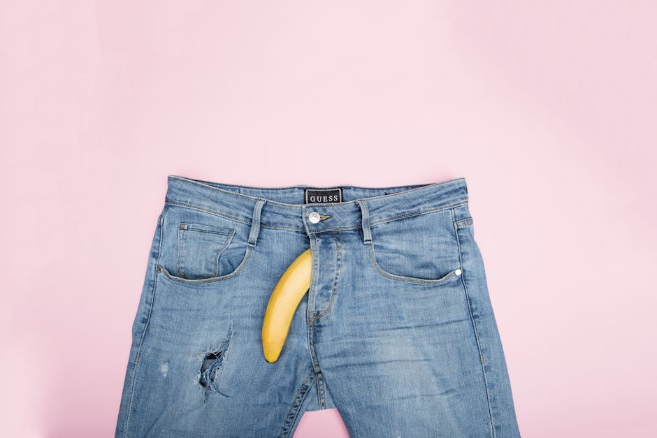 A creative still life featuring blue jeans and a banana against a pink backdrop.