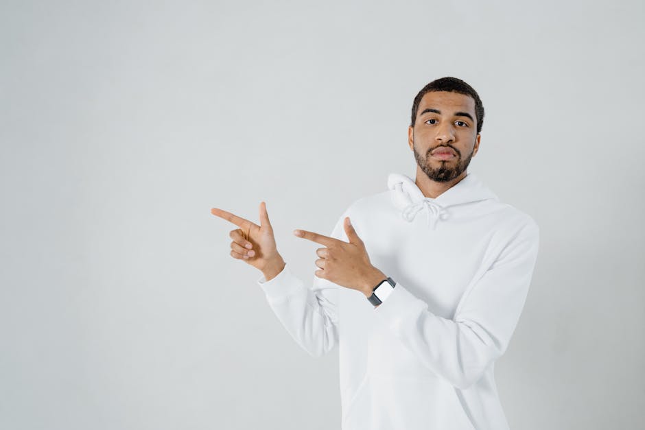 Confident young man in a white hoodie pointing right, studio shot with ample copy space.