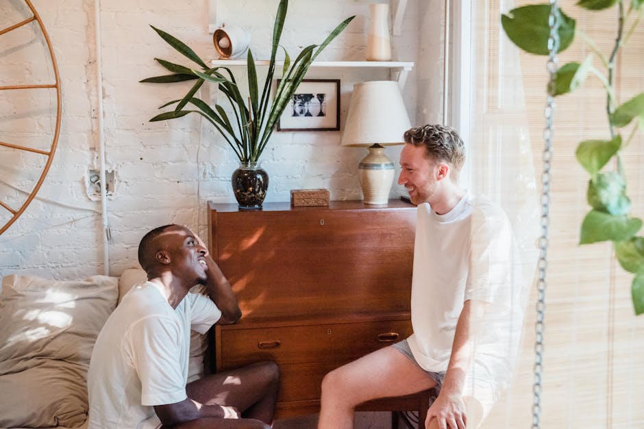 Two men laughing and enjoying a morning together in a cozy bedroom setting.
