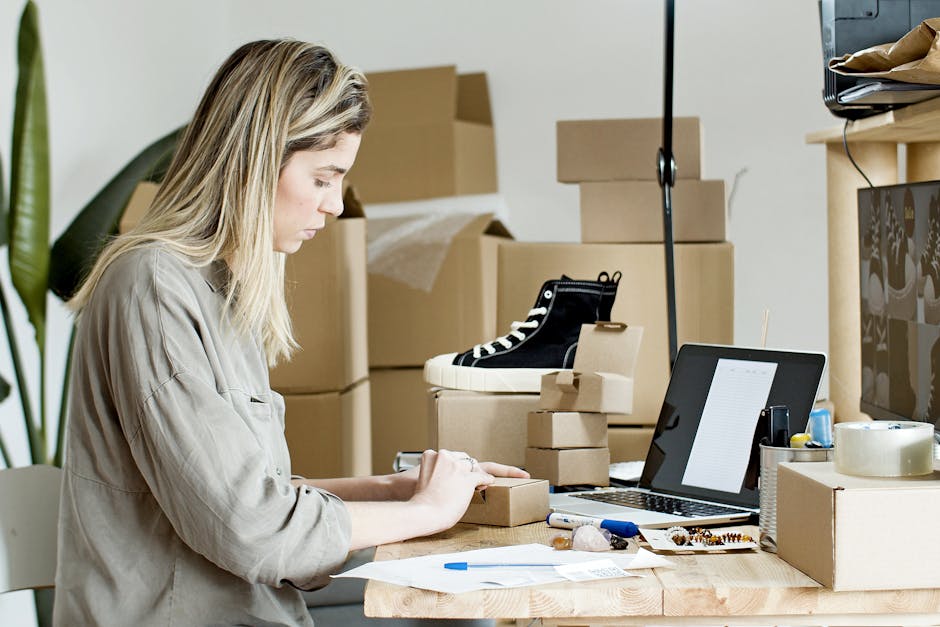 A woman packing boxes for her online store, surrounded by packaging materials and a laptop.
