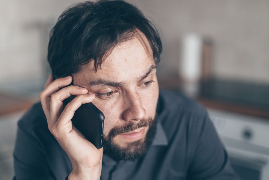 Thoughtful bearded man using smartphone, sitting indoors with a concerned expression.