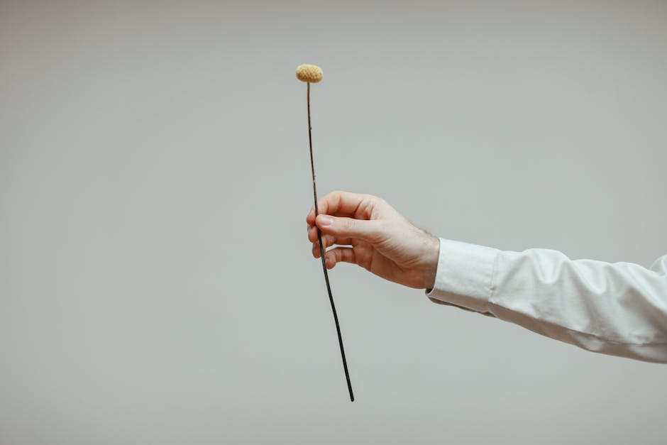 A single yellow flower held delicately by a hand against a neutral background.