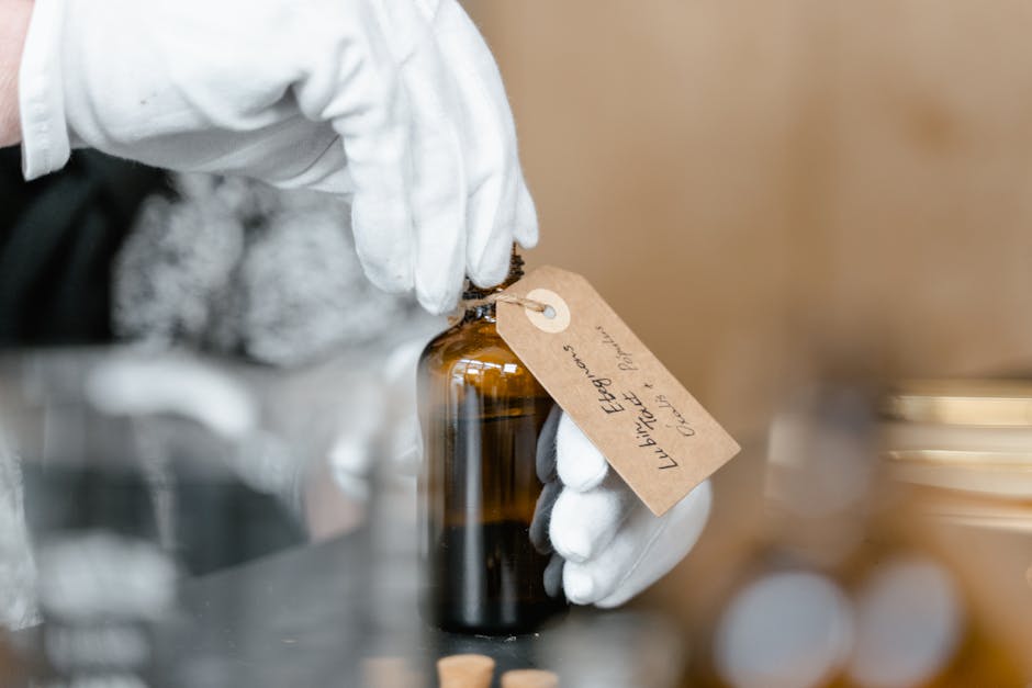 Close-up of a gloved hand holding an elegant glass bottle with a handwritten label for essential oils, showcasing care and precision.
