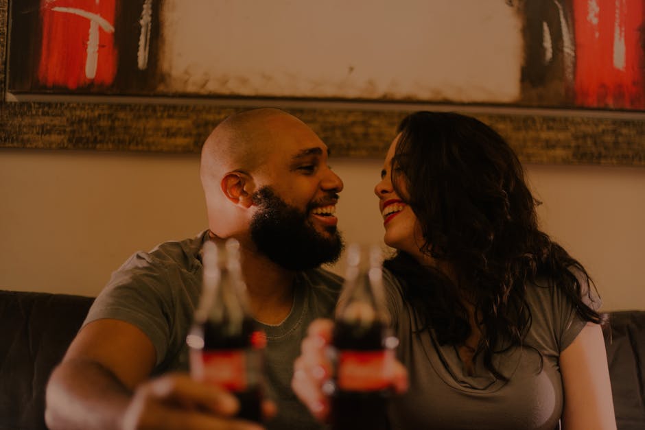 A joyful couple shares a soda and laughter indoors, capturing the essence of love and togetherness.