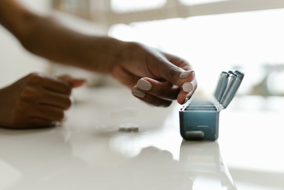 Hand placing pills in a weekly organizer, emphasizing medication management.