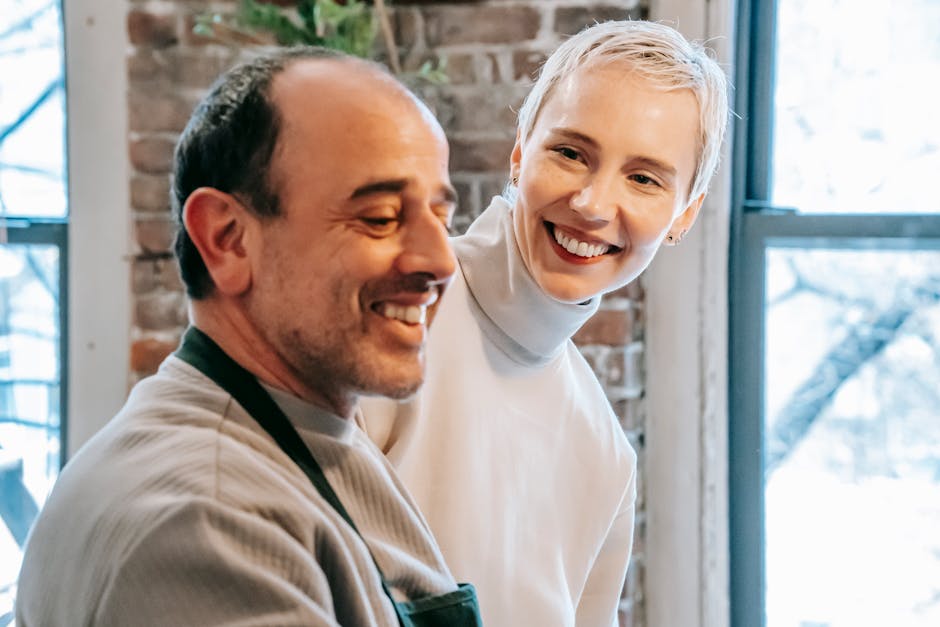 Smiling mature man speaking with charming female beloved while spending weekend together against windows at home
