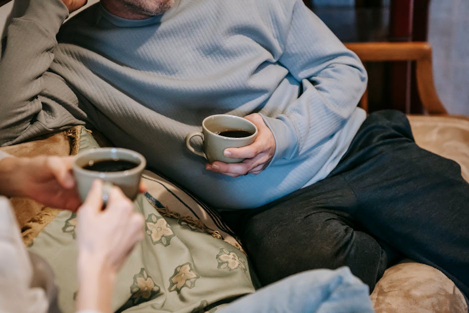 Crop anonymous couple with mugs of tasty aromatic strong coffee on sofa in lounge